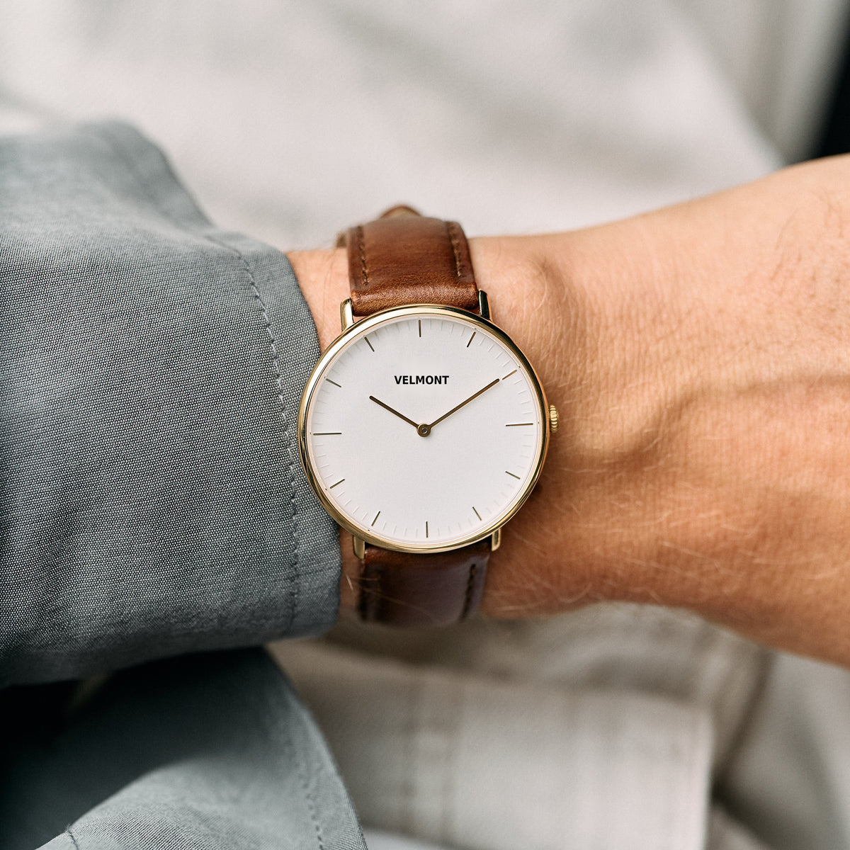 Gold-tone watch on a wrist next to a gray-green shirt sleeve.