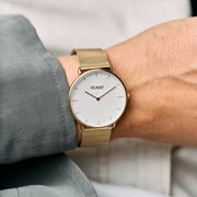 Gold-tone mesh watch worn on a wrist with a sage green shirt cuff.