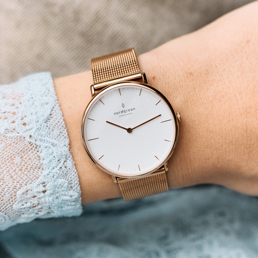 Rose gold-tone mesh watch on a wrist with a pale blue lace sleeve.