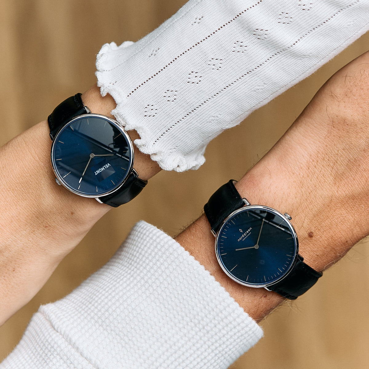 Two matching blue-dial watches on black straps worn by a couple, wrists crossed.