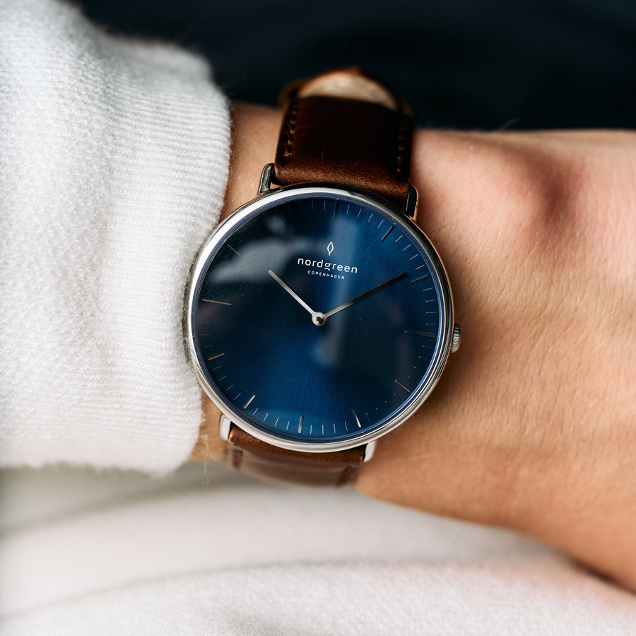 Blue sunburst dial in a silver-tone case, worn on a brown strap with a white sweater.