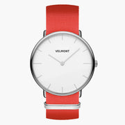 Minimalist watch with a white dial and silver-tone case on a bright red woven strap.