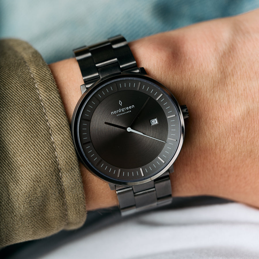 Gray-dial watch worn on a wrist next to an olive jacket cuff.