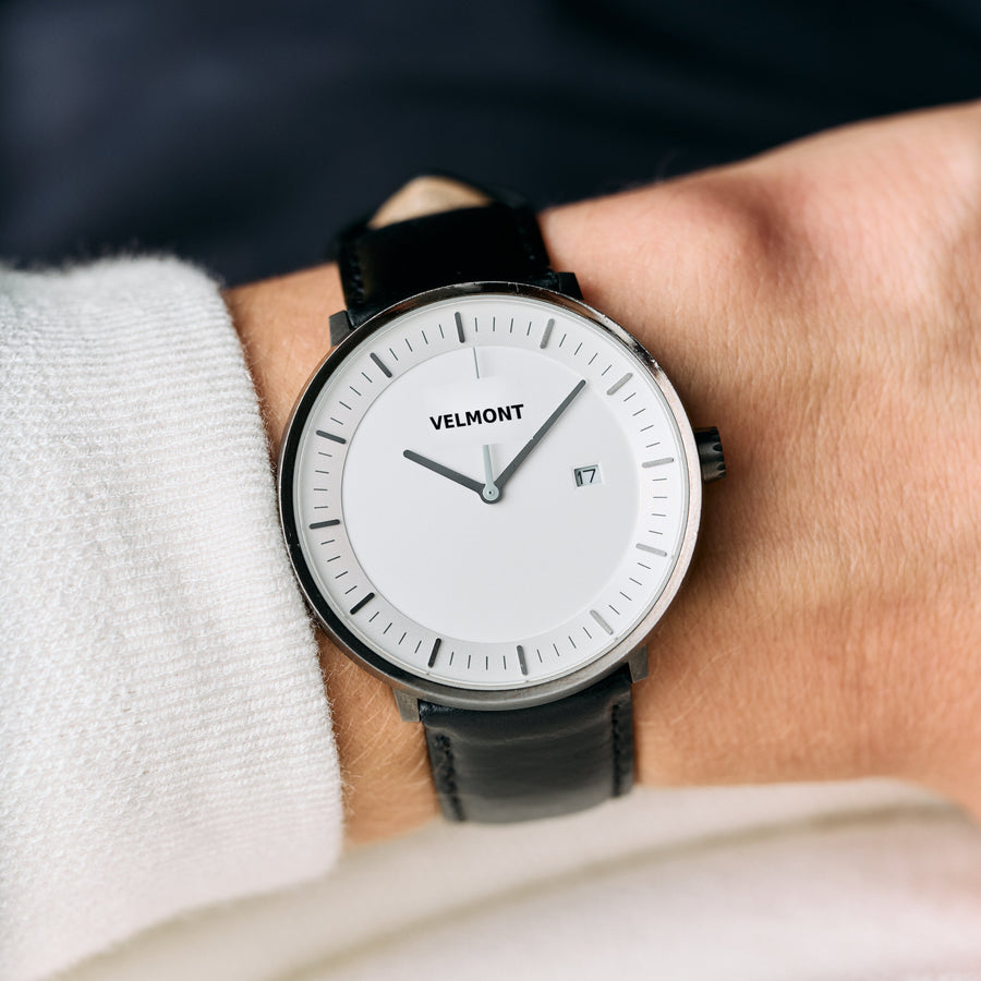 The gunmetal watch with a white dial, worn on a black strap with a cream sweater.