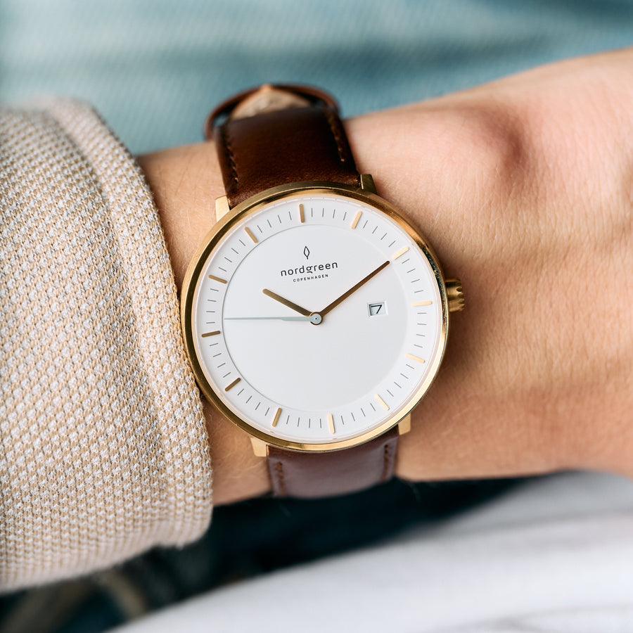 Gold-tone case and white dial on a brown strap, worn with a beige knit sleeve.