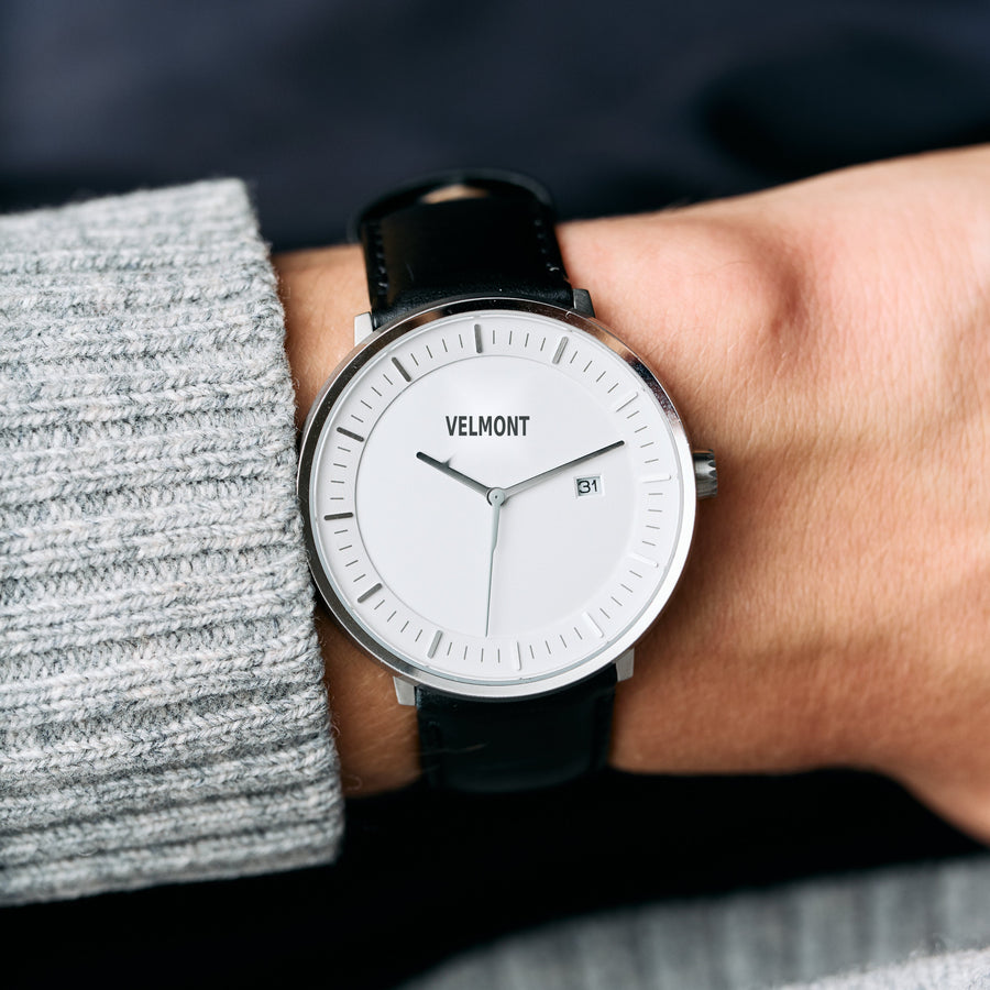 White dial and silver-tone case on a black strap, worn under a gray knit cuff.