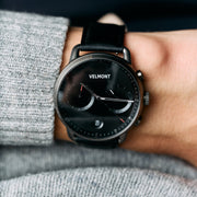 The all-dark watch worn on a wrist beside a gray knit sweater.