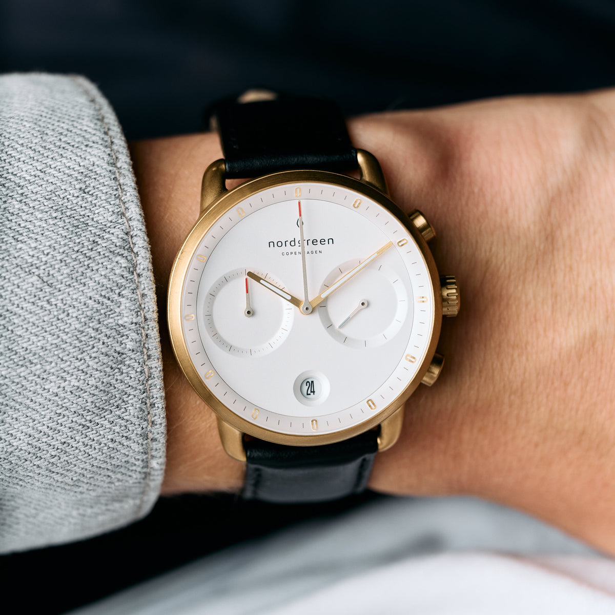 The gold-tone watch worn on a wrist beside a gray twill sleeve.