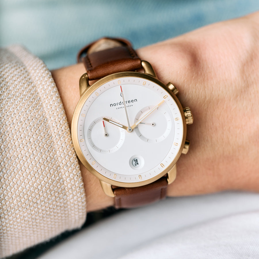 The watch worn on a wrist next to a beige knit sleeve.