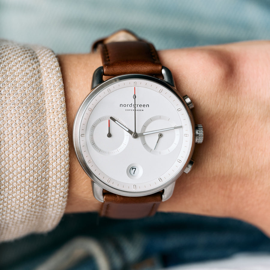 The watch on a wrist with a beige knit sleeve, subdials facing the camera.