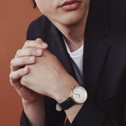 Man in a dark blazer with clasped hands, wearing the rose gold-tone watch.