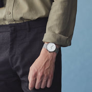 Man in an olive shirt and dark trousers wearing the watch, seen from the side.