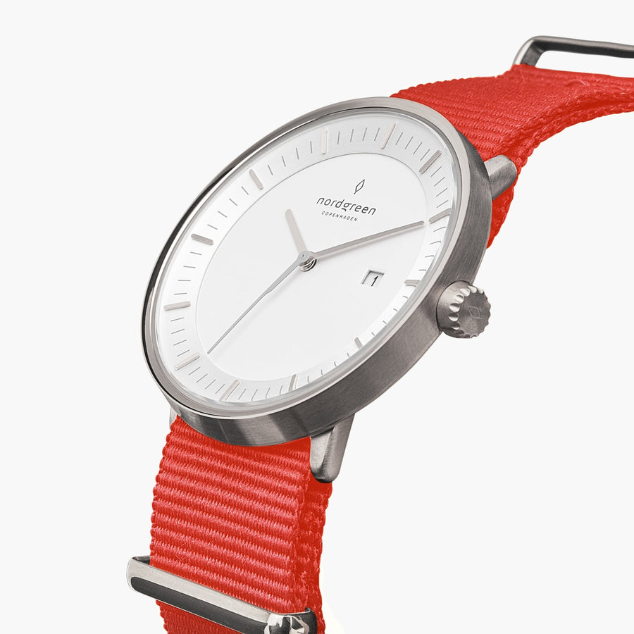Three-quarter view of the silver-tone case and date window on a red fabric strap.