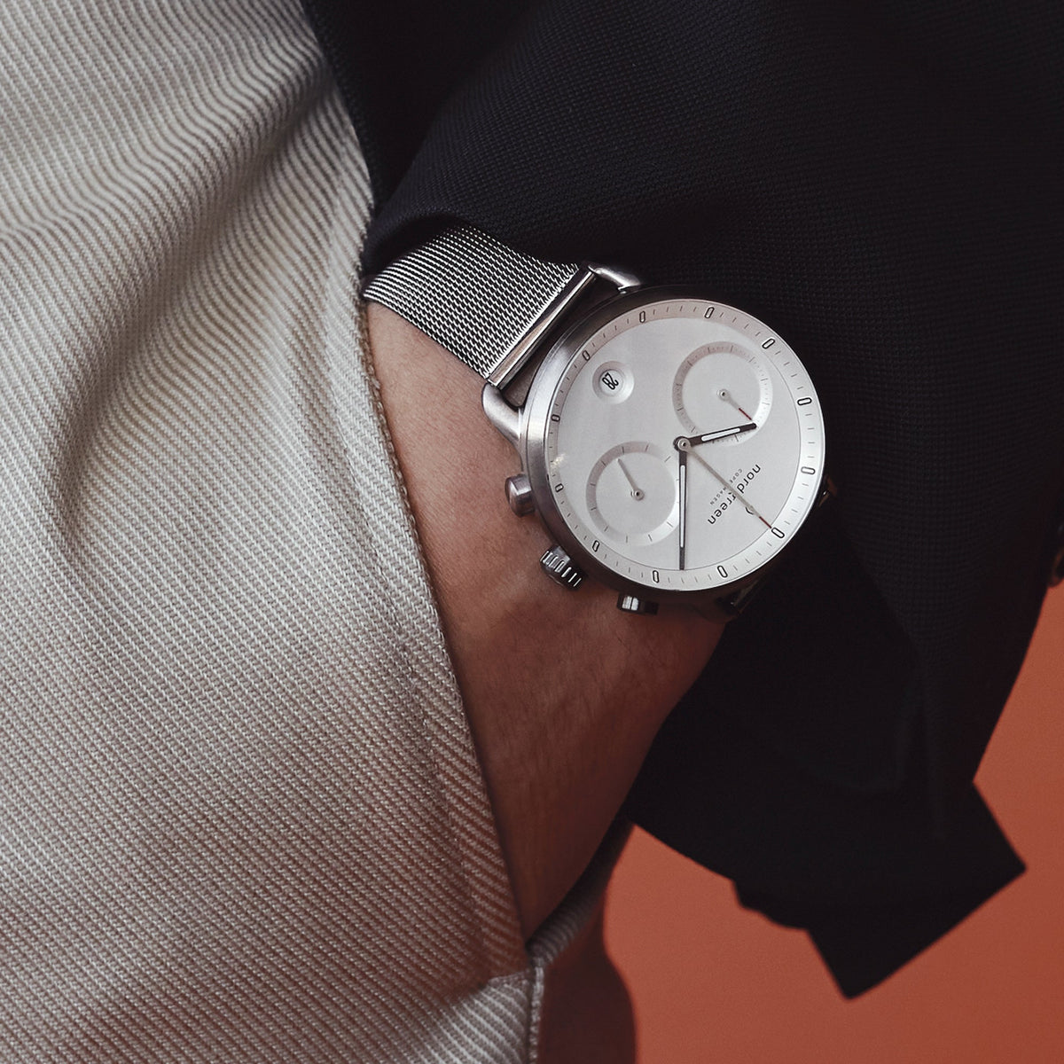 Hand resting in a beige trouser pocket, wearing the white dial mesh watch.