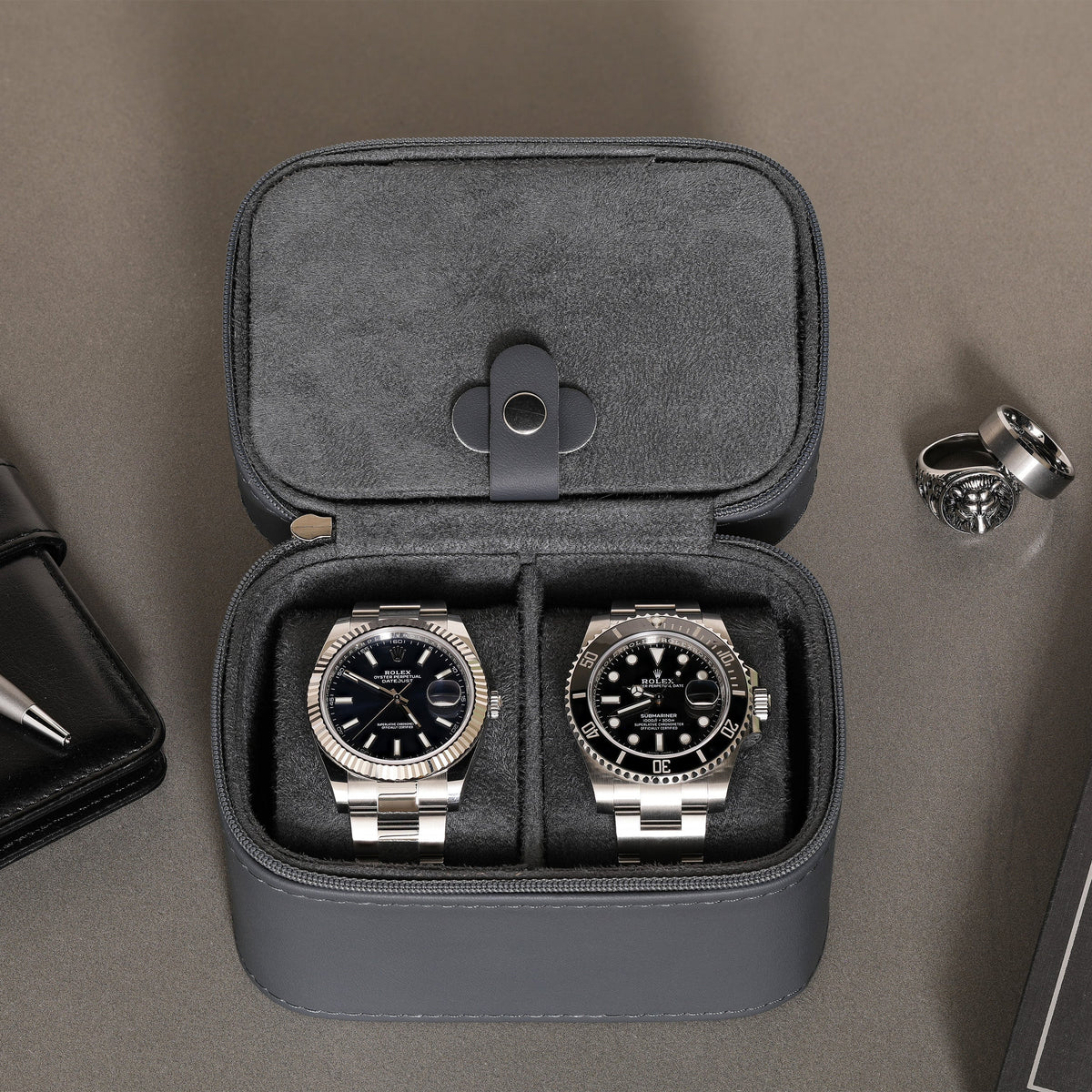 Two watches in the open travel case with a ring beside it