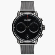 Chronograph-style watch with a black dial and gunmetal case on a matching mesh strap, front view.