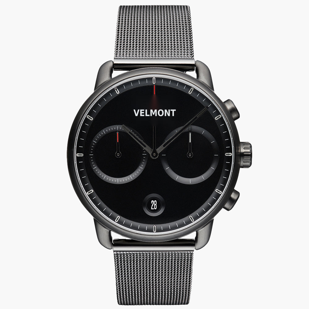 Chronograph-style watch with a black dial and gunmetal case on a matching mesh strap, front view.