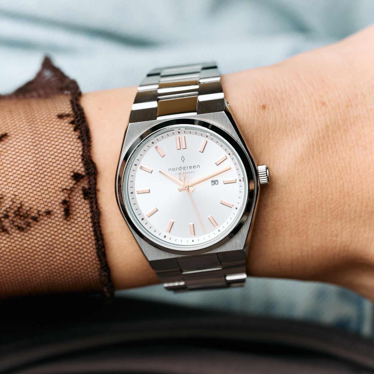 The silver-tone watch on a wrist under a sheer black lace sleeve.