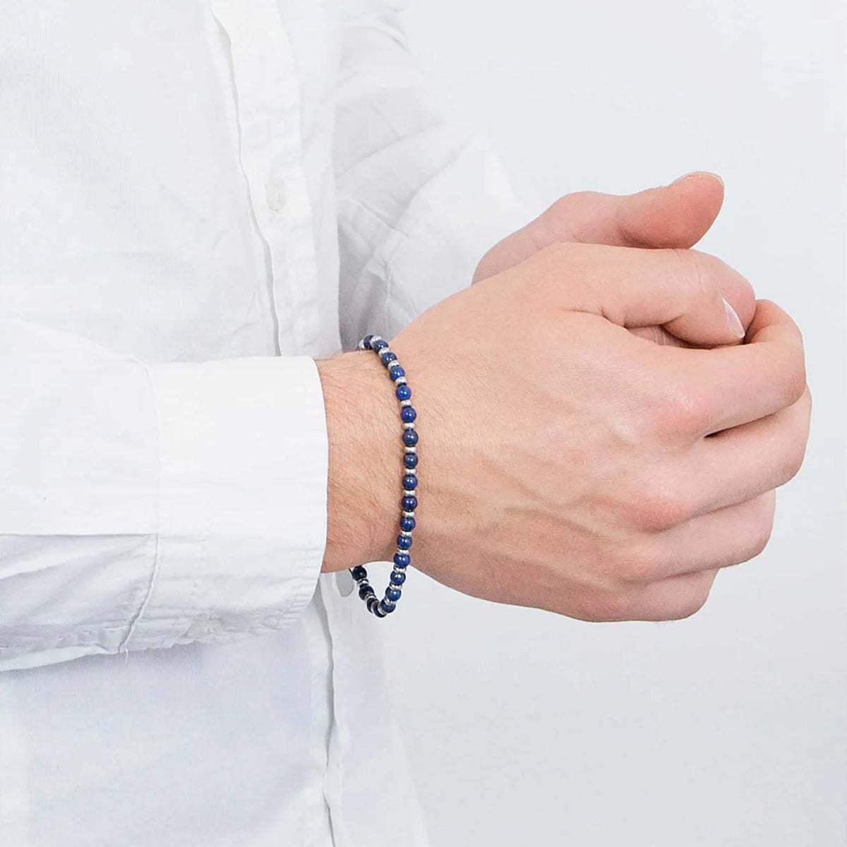 Beaded bracelet worn with a white shirt, hands clasped