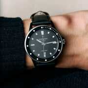 Diver-style watch on a smooth black strap, worn with a dark sleeve.