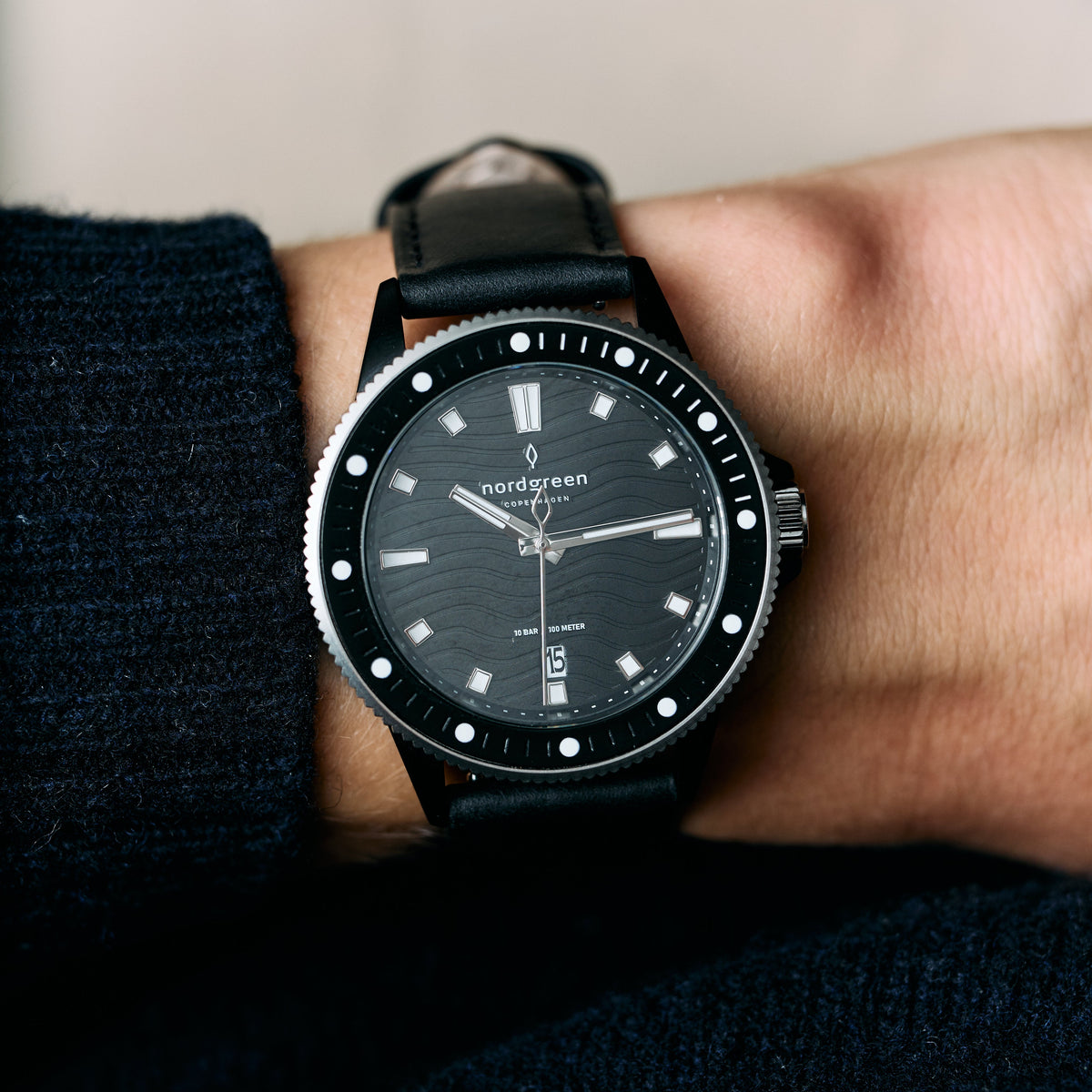 Diver-style watch on a smooth black strap, worn with a dark sleeve.