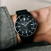 The black watch worn on a wrist beside a gray sleeve.