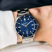 Blue dial bracelet watch worn on a wrist next to a white sleeve.