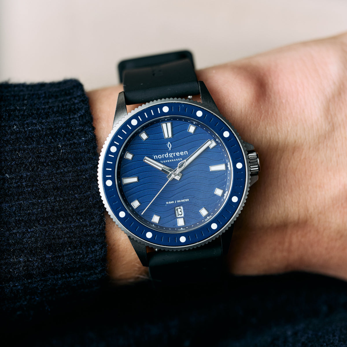 The blue-dial watch worn on a wrist beside a navy knit sleeve.