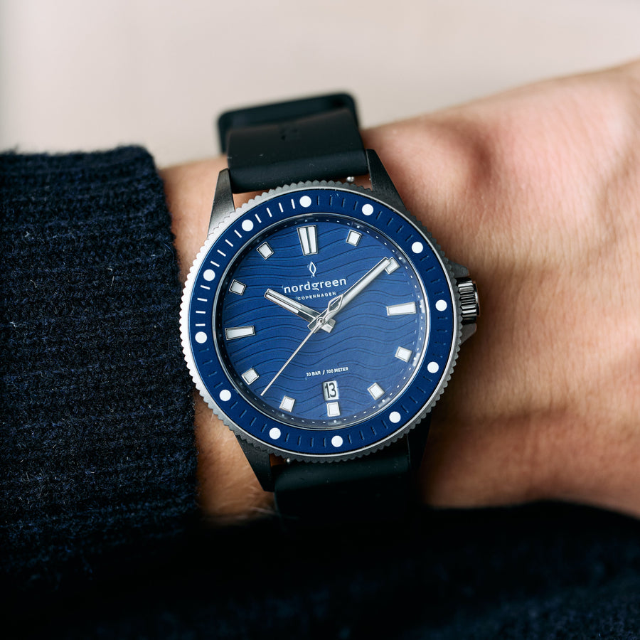 The blue-dial watch worn on a wrist beside a navy knit sleeve.