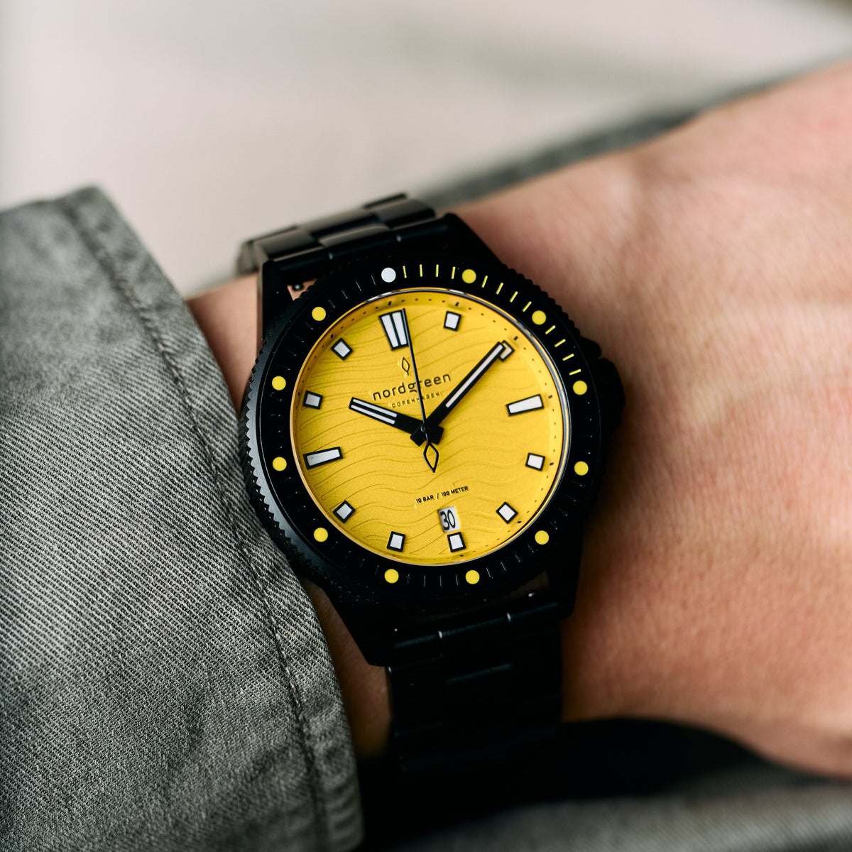 The black and yellow watch worn on a wrist under a gray shirt cuff.