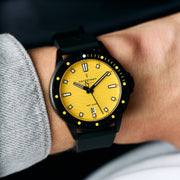 The yellow-dial watch worn on a wrist beside a gray sweater cuff.