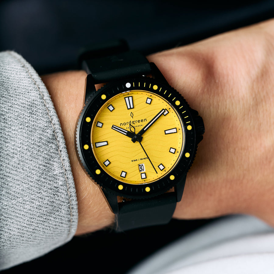 The yellow-dial watch worn on a wrist beside a gray sweater cuff.