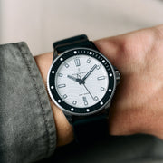 The white-dial watch worn on a wrist next to a gray knit sleeve.