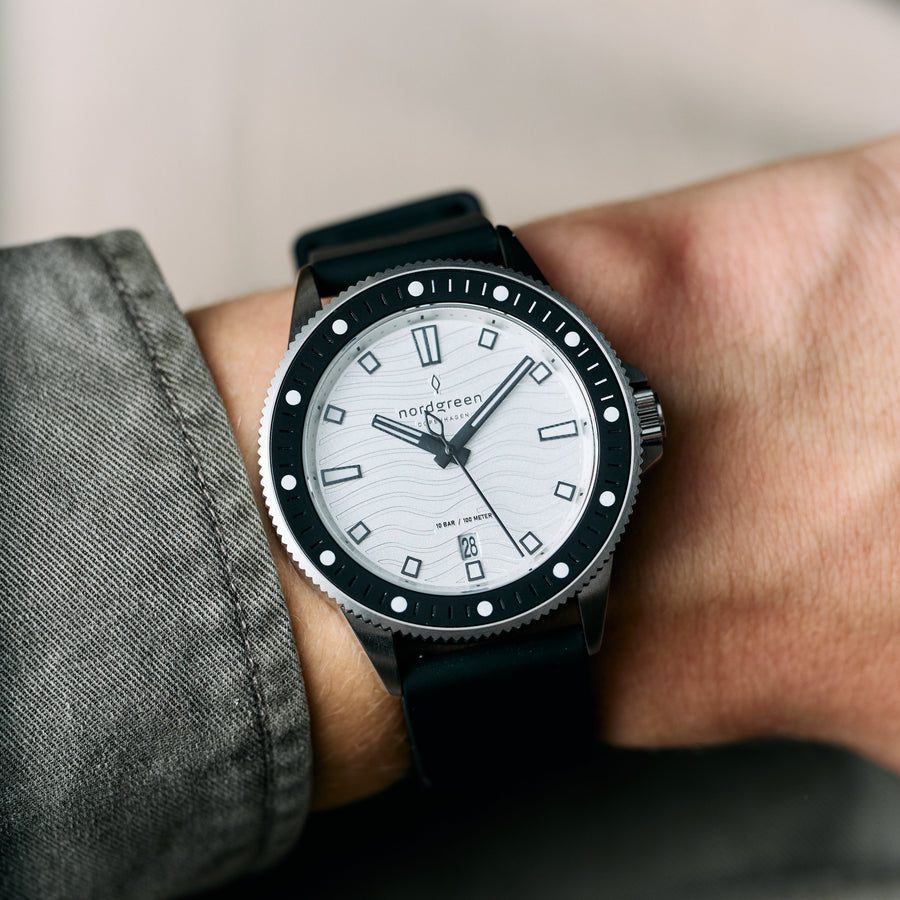 The white-dial watch worn on a wrist next to a gray knit sleeve.