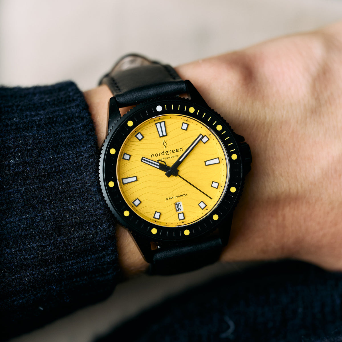 The yellow-dial watch worn on a wrist beside a dark knit sleeve.