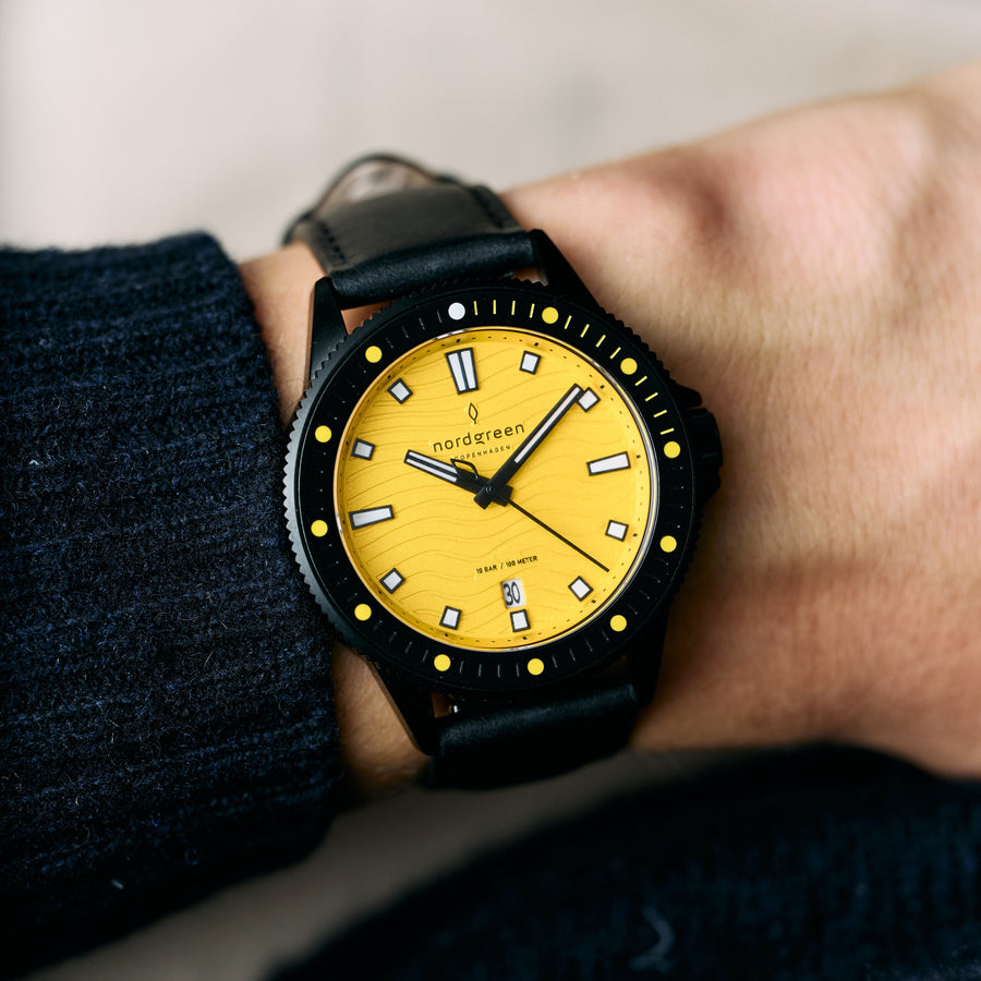 The yellow-dial watch worn on a wrist beside a dark knit sleeve.
