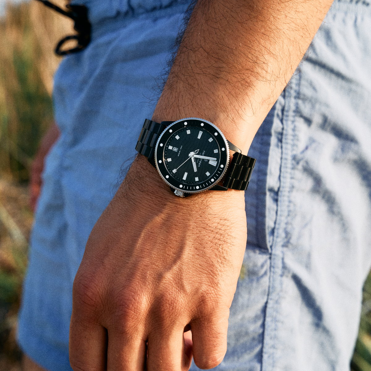 The black watch on a black link bracelet, worn with light blue shorts.