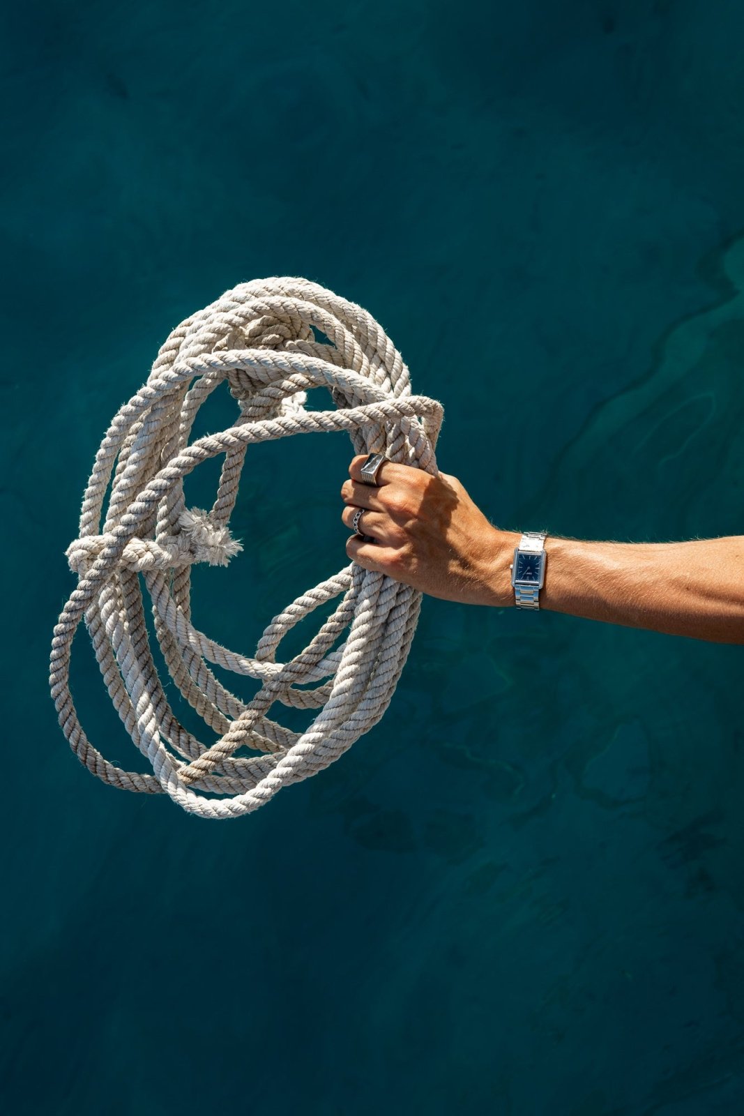 Arm holding a coiled rope over water, watch on the wrist