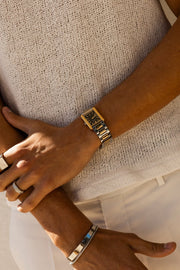 Arms crossed, gold-tone rectangular watch on the wrist