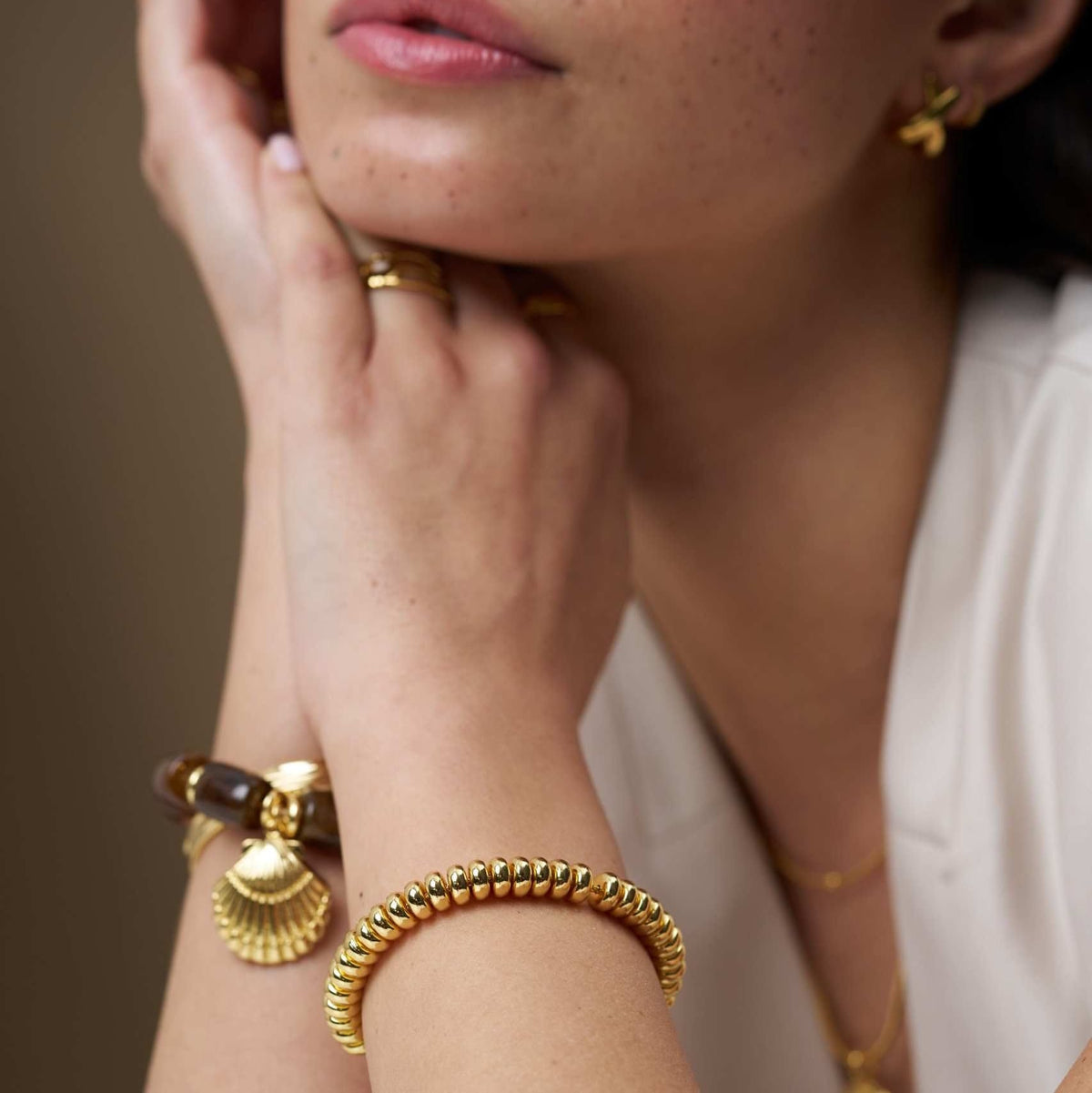 Gold-tone nugget bracelet worn with a shell charm bracelet