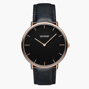 Watch with a black dial and rose gold-tone case on a black strap, shown from the front.