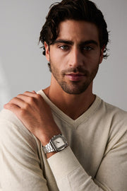 Man in a cream sweater, hand on shoulder, wearing the square watch