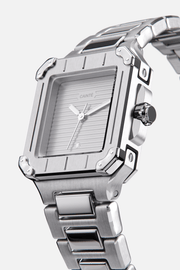 Angled view of the square case with screw details at the corners and gray dial