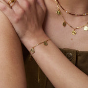 Coin charm bracelet worn with layered necklaces