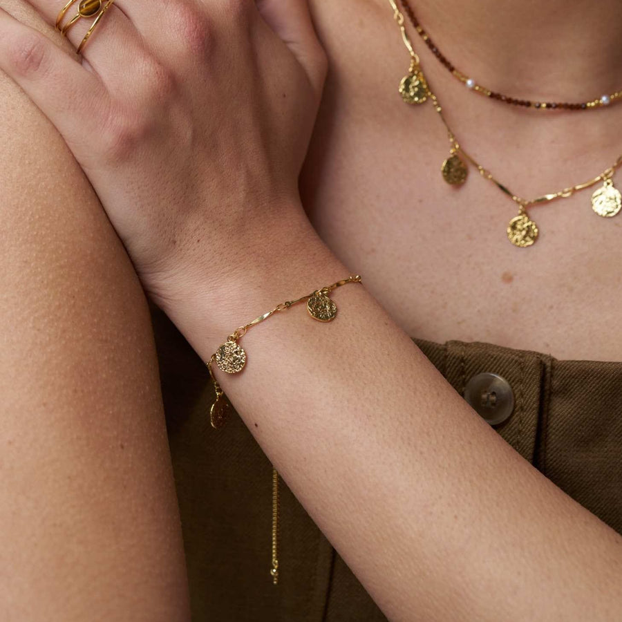 Coin charm bracelet worn with layered necklaces