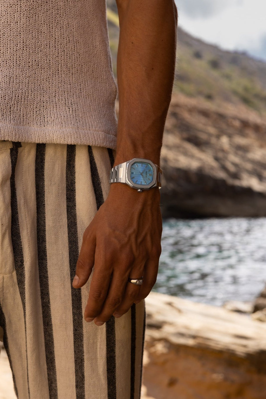 Man in striped trousers by sea rocks wearing the watch