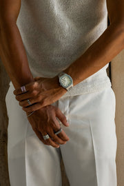 Hands crossed in front of white trousers, watch visible