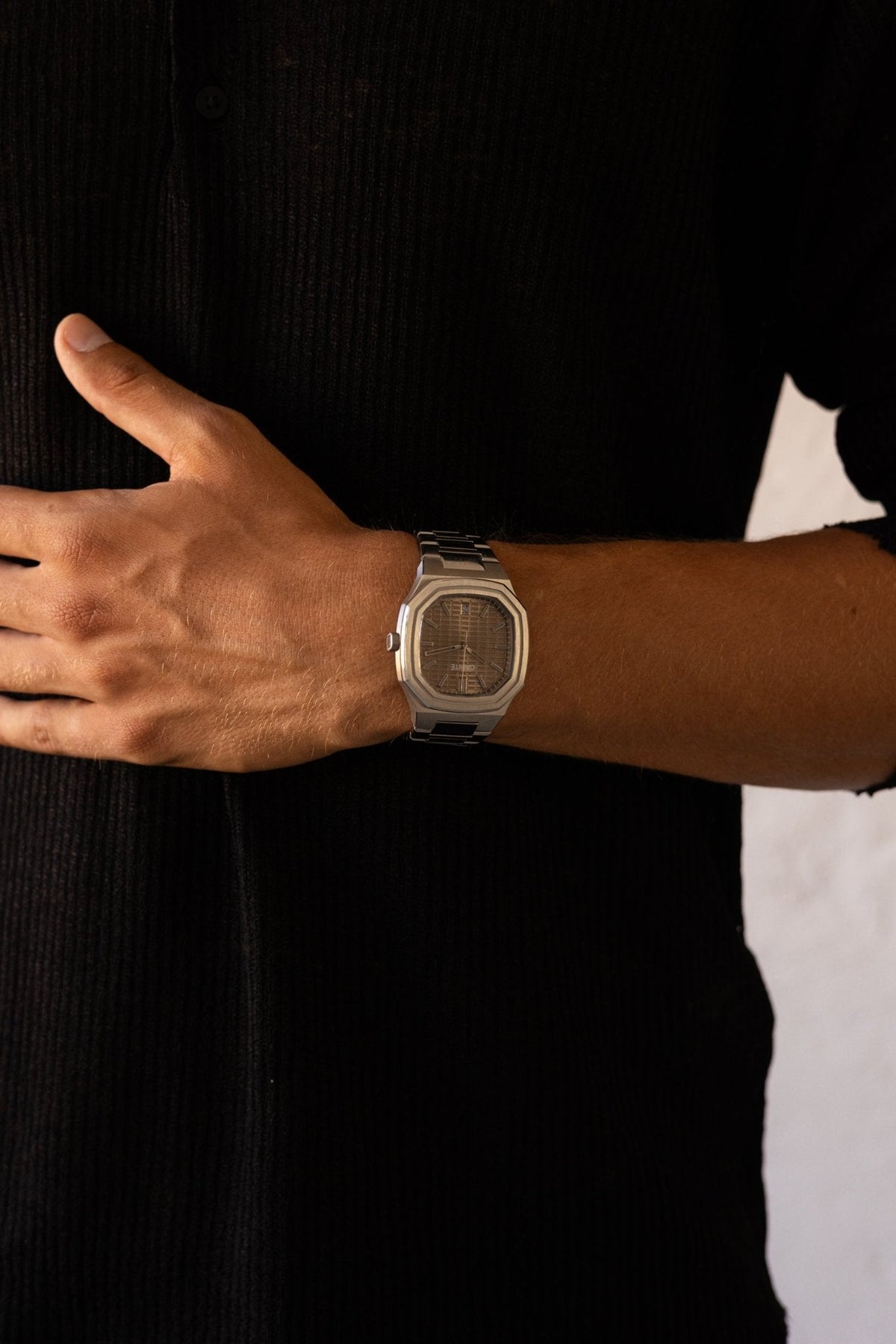 Hands crossed over a black shirt, watch visible