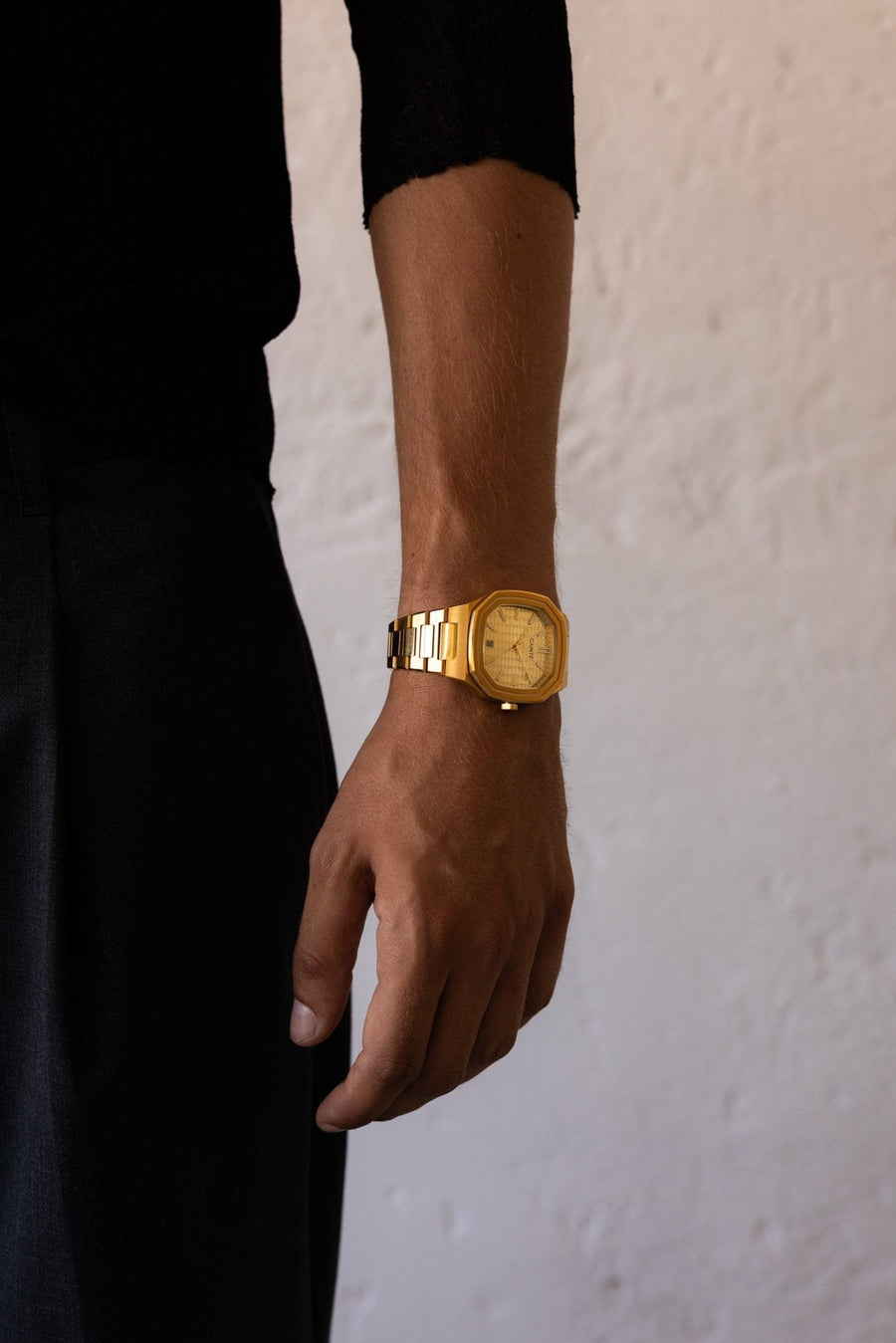 Man in black standing by a white wall, watch on the wrist