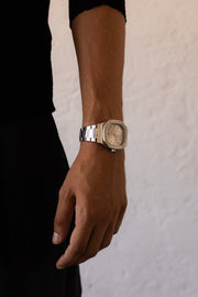 Man in black standing by a white wall, watch on the wrist